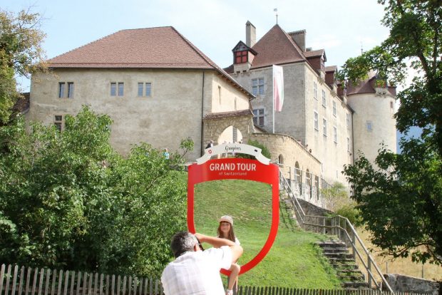 Un homme prend sa fille en photo dans le cadre photo «Grand Tour» posé devant le Château de Gruyères 